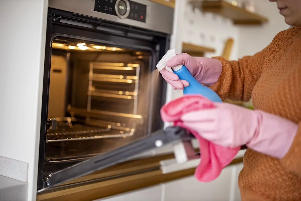 young-woman-cleaning-oven-with-rag-kitchen